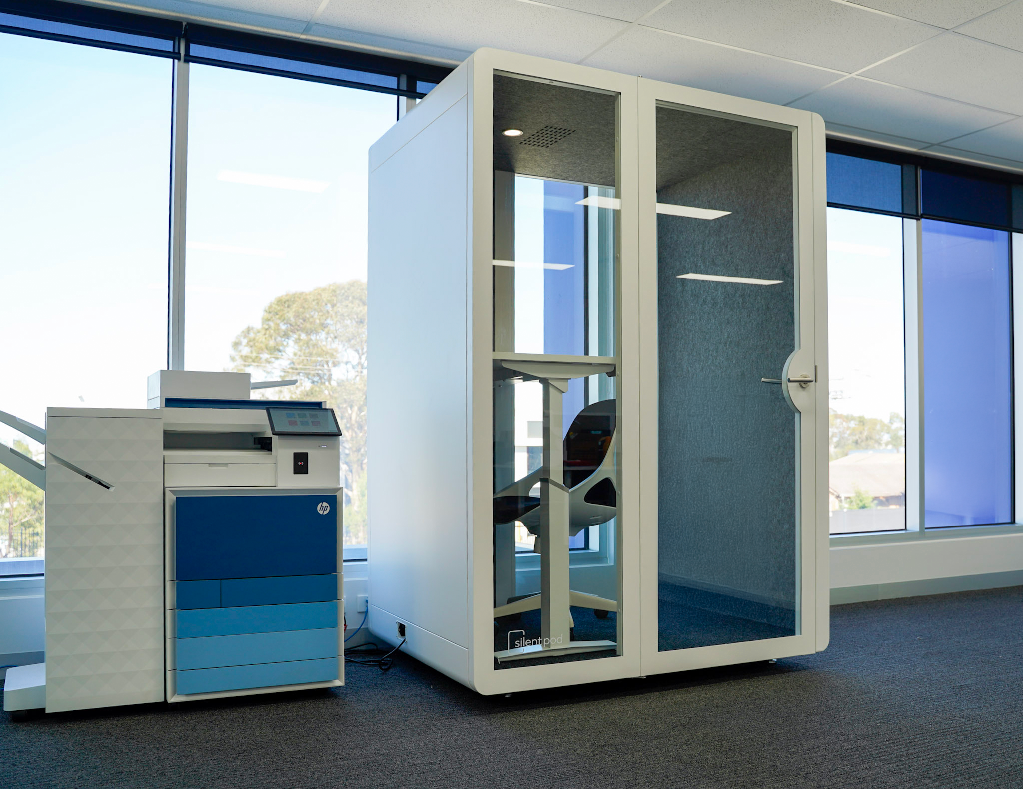 White acoustic meeting pod installed beside a printer in a bright Melbourne office with large windows.