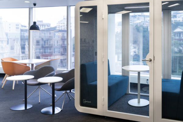 A modern office with a glass-fronted acoustic pod beside a lounge area with soft seating and city views.