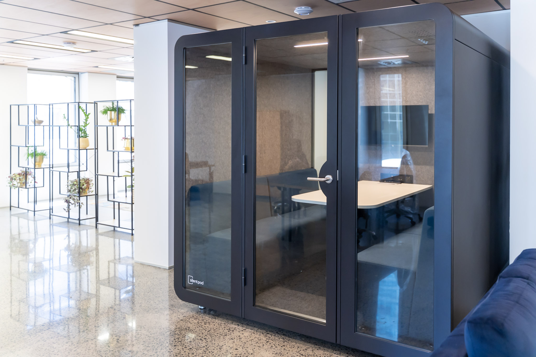 Black Silent Pod boardroom pod with built-in screen and seating for 4–6 people, positioned in a modern open-plan office.
