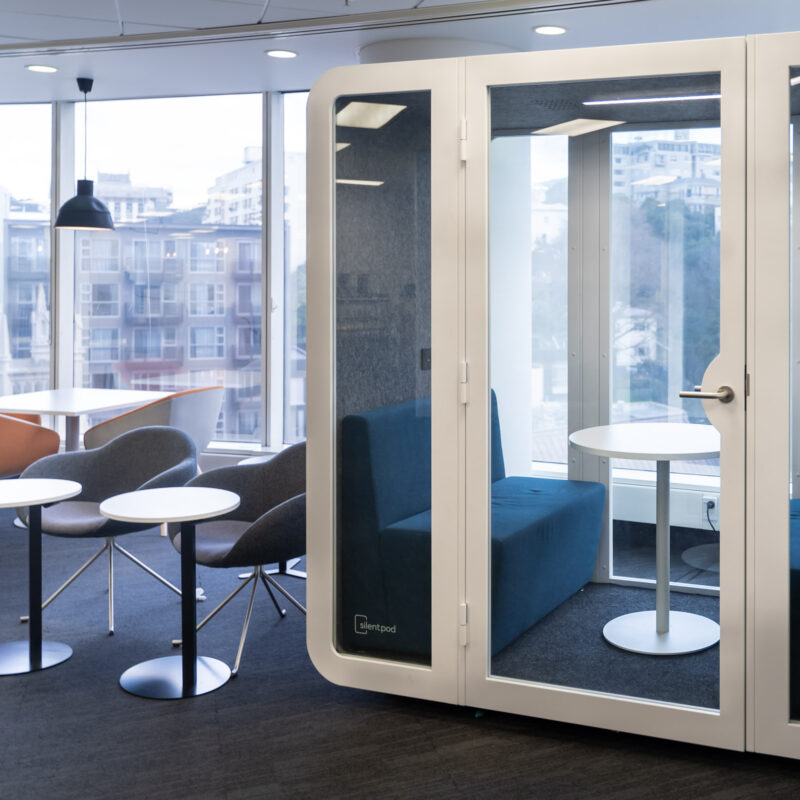 Collab Pod set up in a bright office lounge, with blue sofas and a round table inside for team discussions.