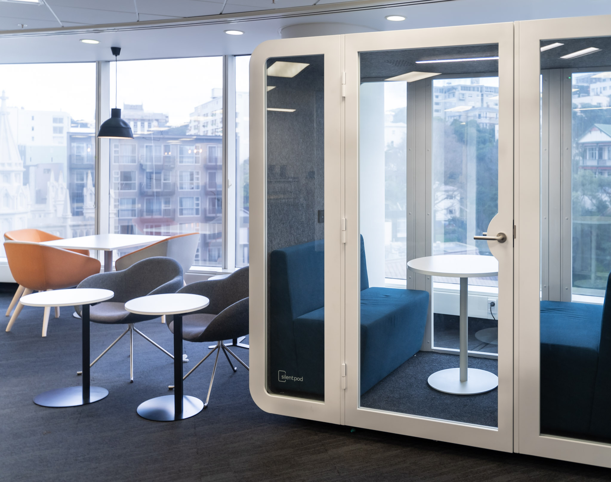 Collab Pod set up in a bright office lounge, with blue sofas and a round table inside for team discussions.