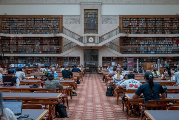 Students in a busy library, working on laptops and using headphones to drown out noise.