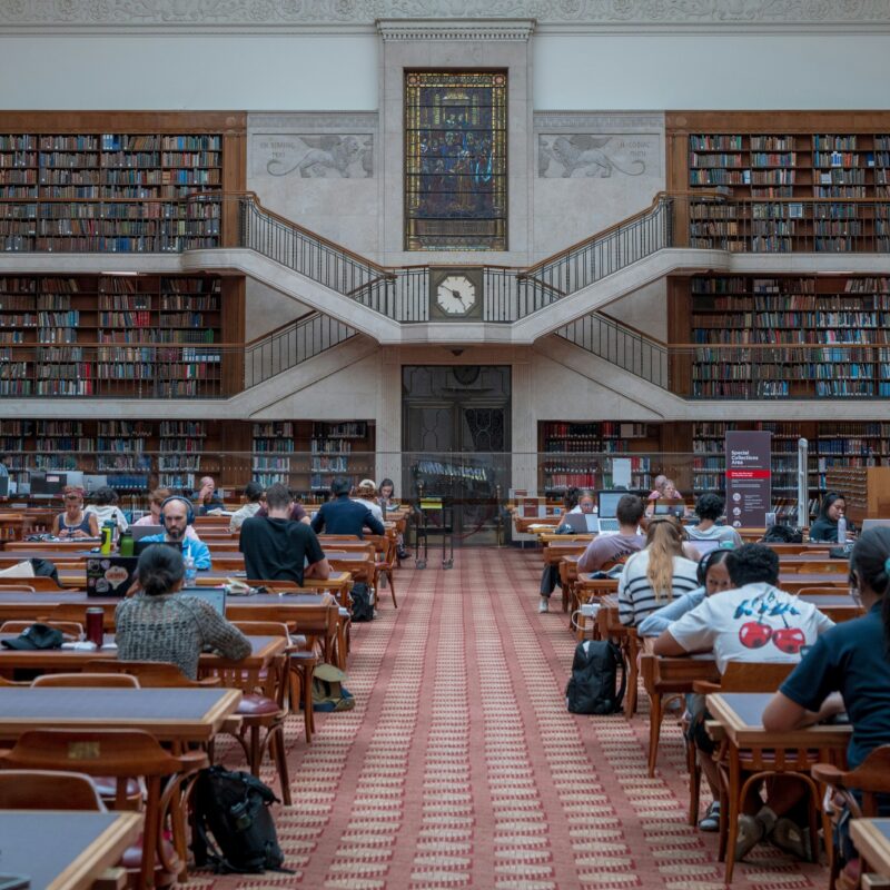 Students in a busy library, working on laptops and using headphones to drown out noise.