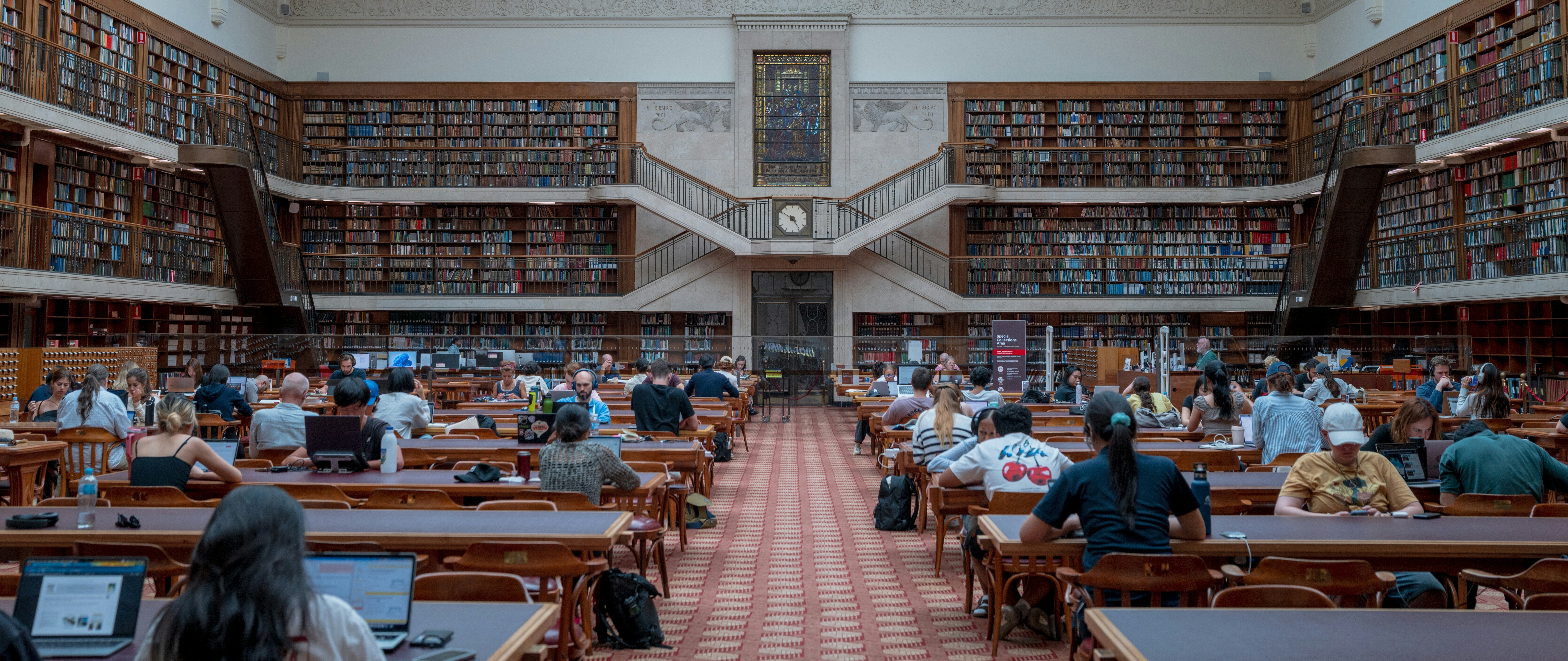 Students in a busy library, working on laptops and using headphones to drown out noise.